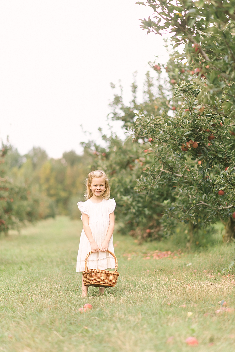 Little girl in cream colored dress holding a basket of apples | Photo by Jessica Lee Photography