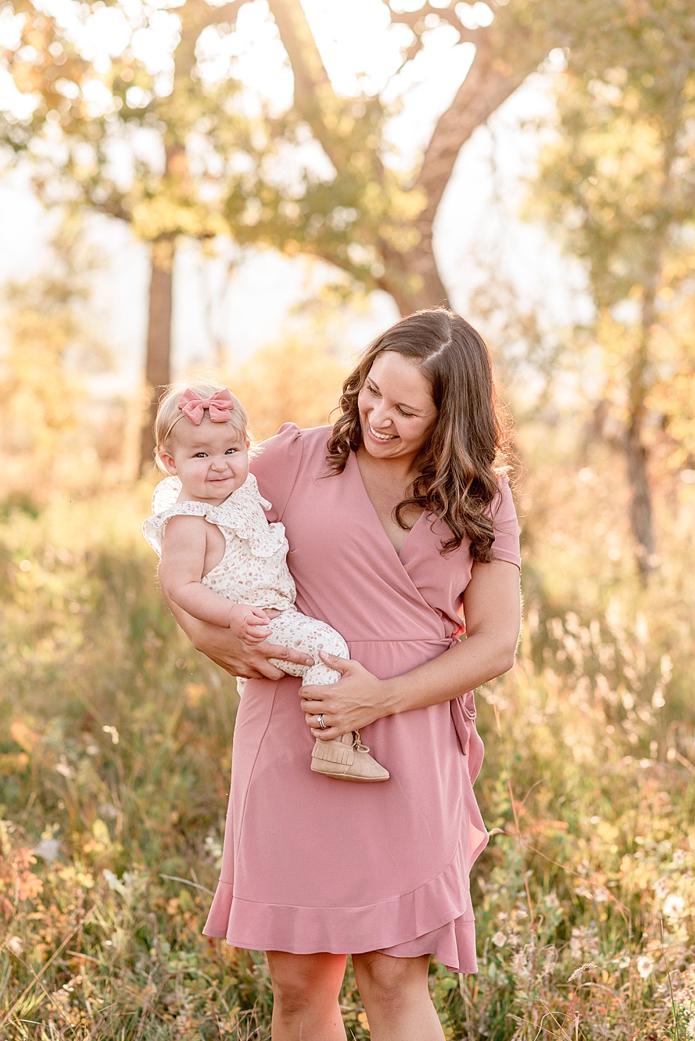 Mom in pink dress smiling and holding baby girl | Photo by Jessica Lee Photography