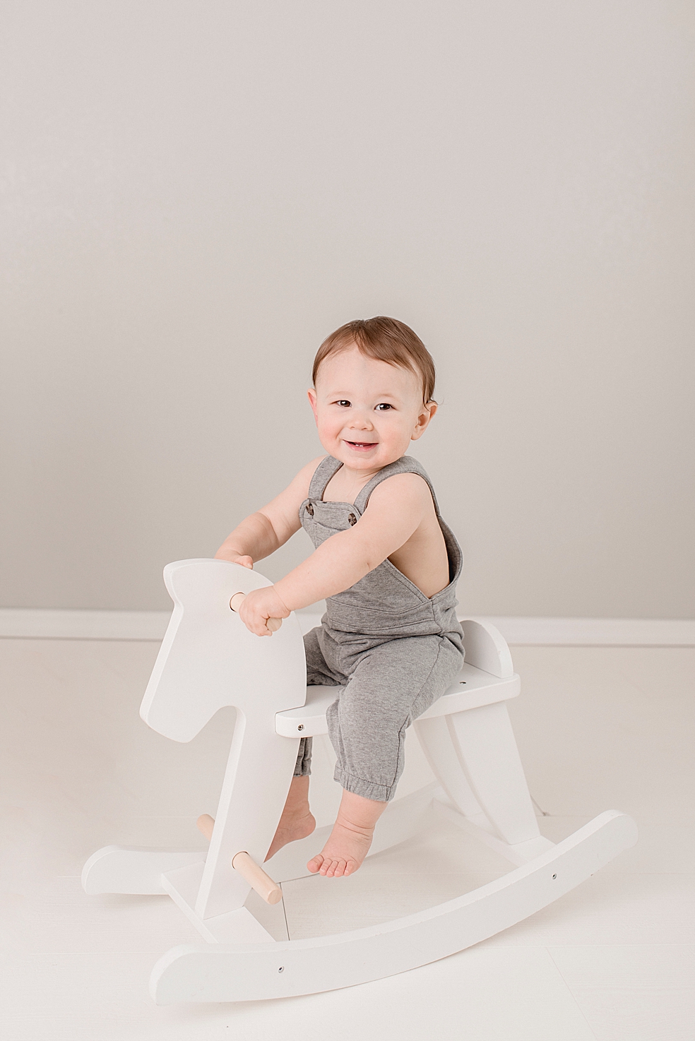 Baby boy in gray jumper sitting on white rocking horse | Photo by Jessica Lee Photography