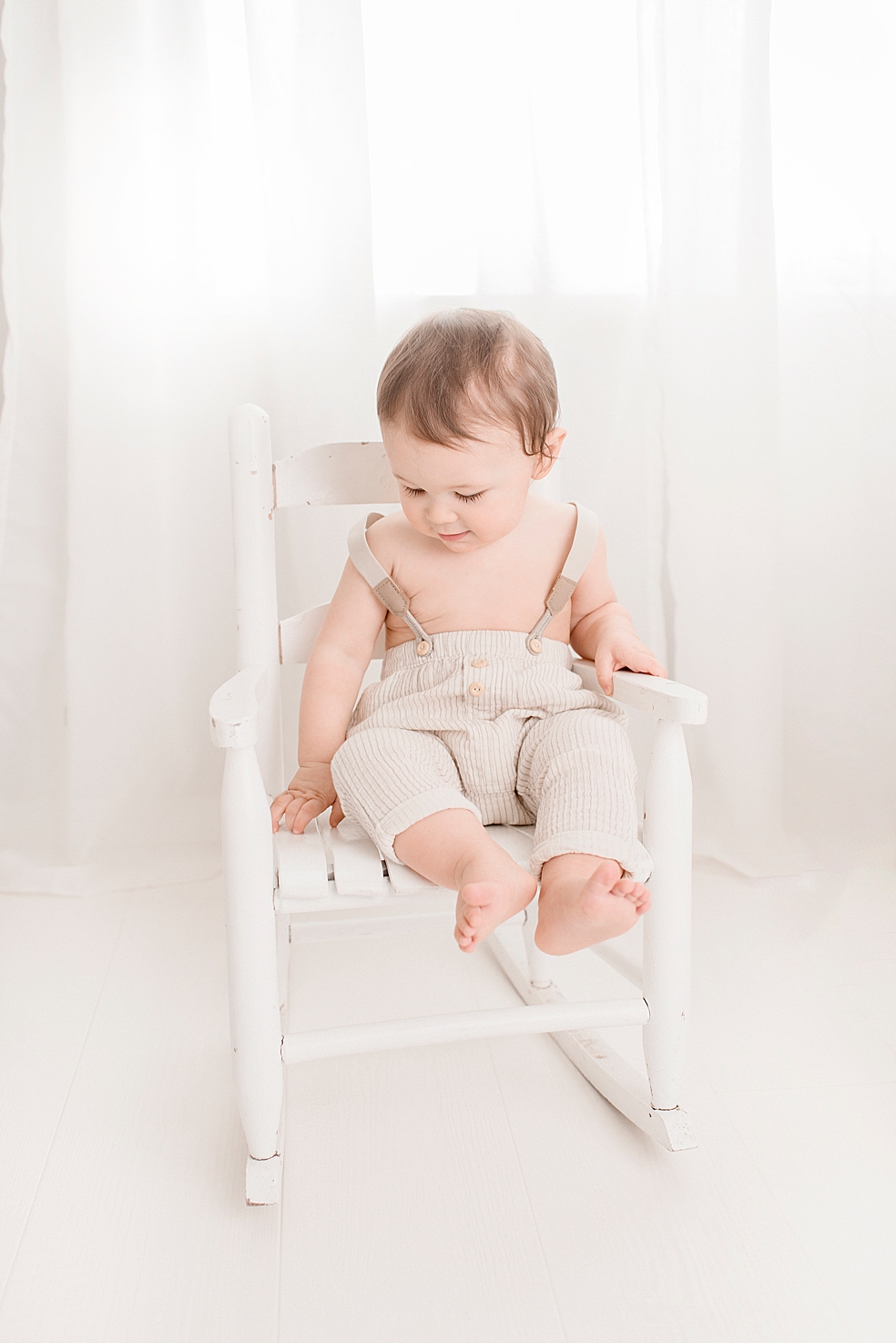 Toddler boy in overalls sitting in white rocking chair | Photo by Huntsville Baby Photographer Jessica Lee 