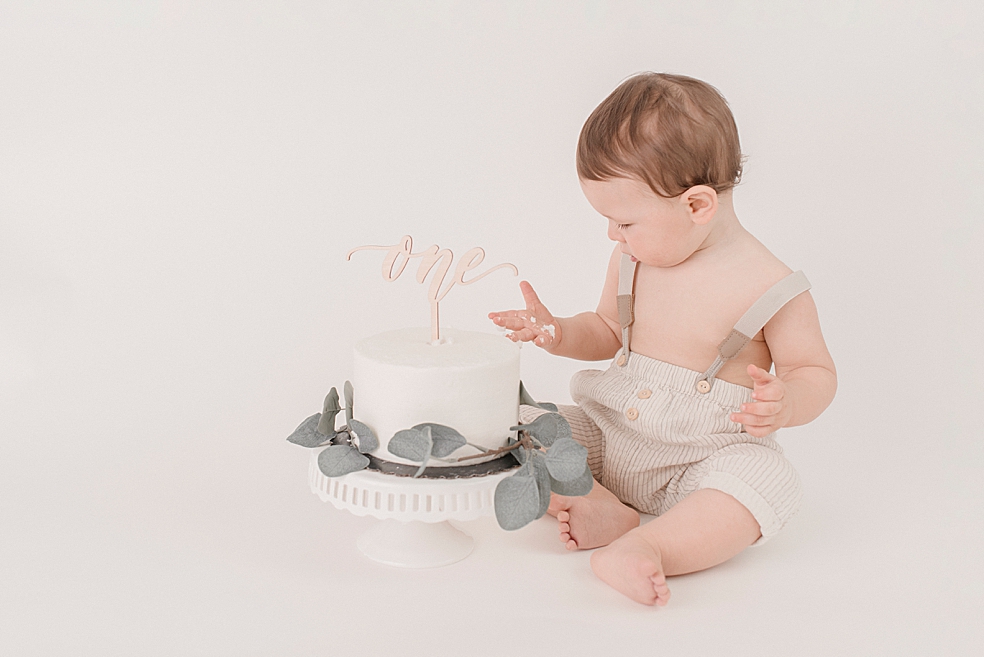 Baby boy playing with smash cake with "one" sign | Photo by Huntsville Baby Photographer Jessica Lee 