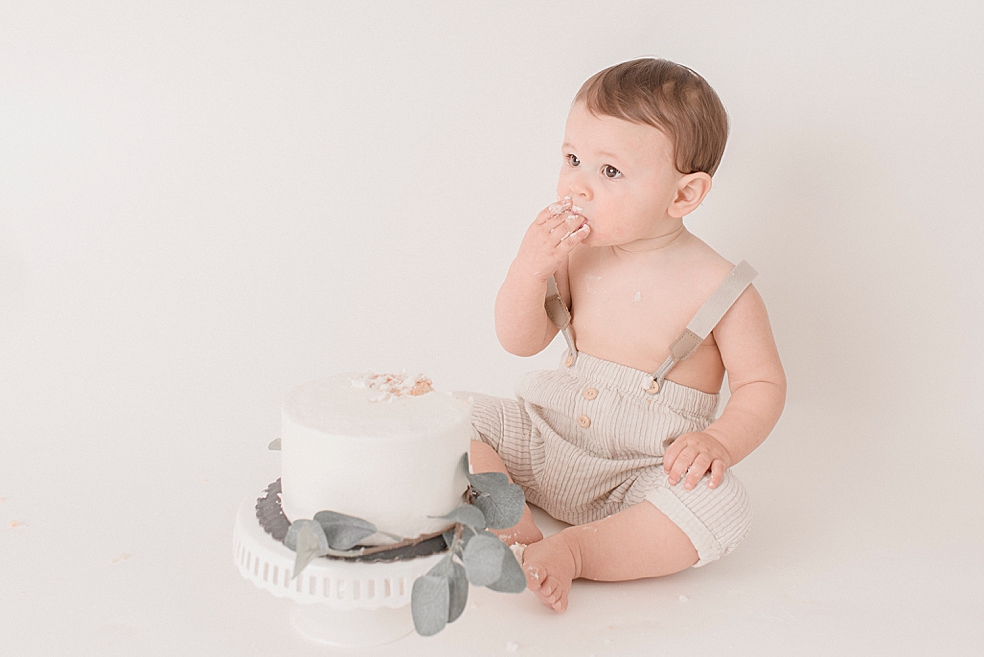 Baby boy in striped tan overalls eating smash cake | Photo by Jessica Lee Photography