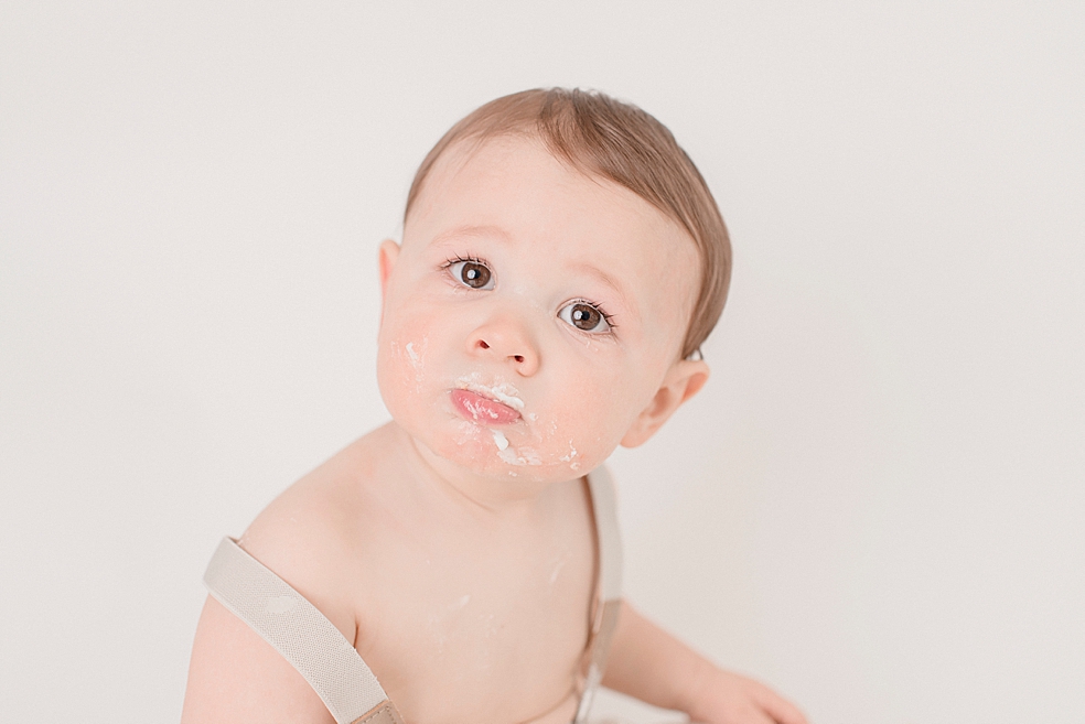 Toddler baby boy in overalls eating cake | Photo by Huntsville Baby Photographer Jessica Lee 