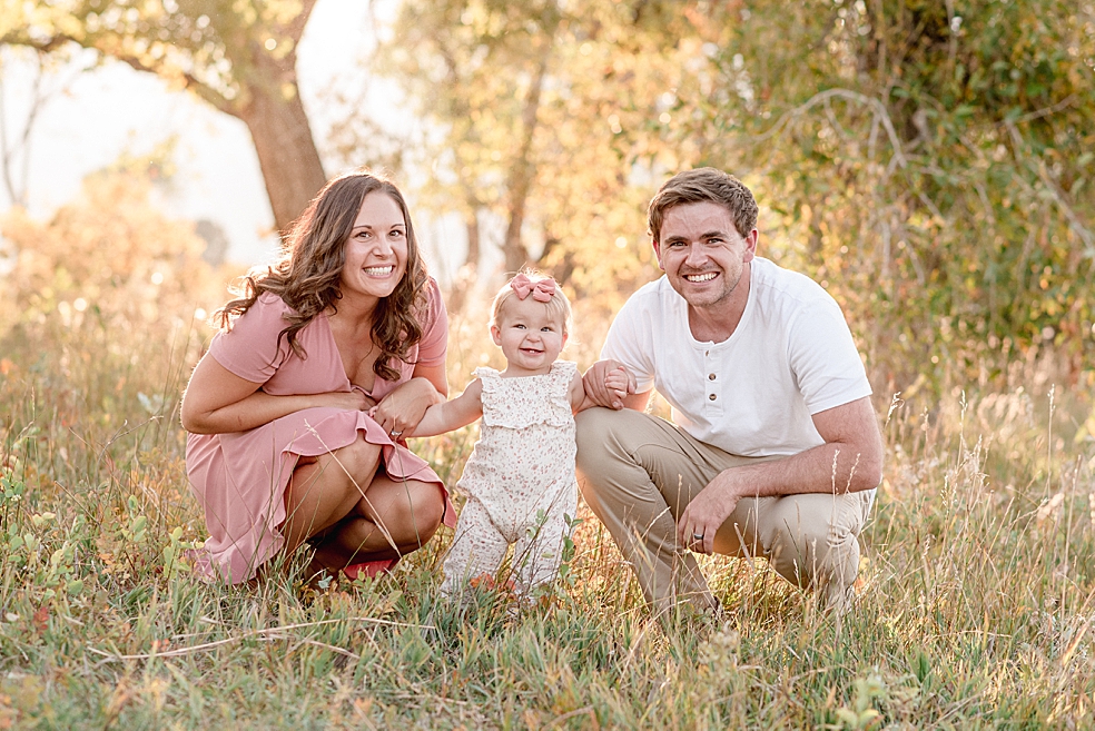 Mom in pink and dad in white crouching beside toddler baby girl | Photo by Jessica Lee Photography