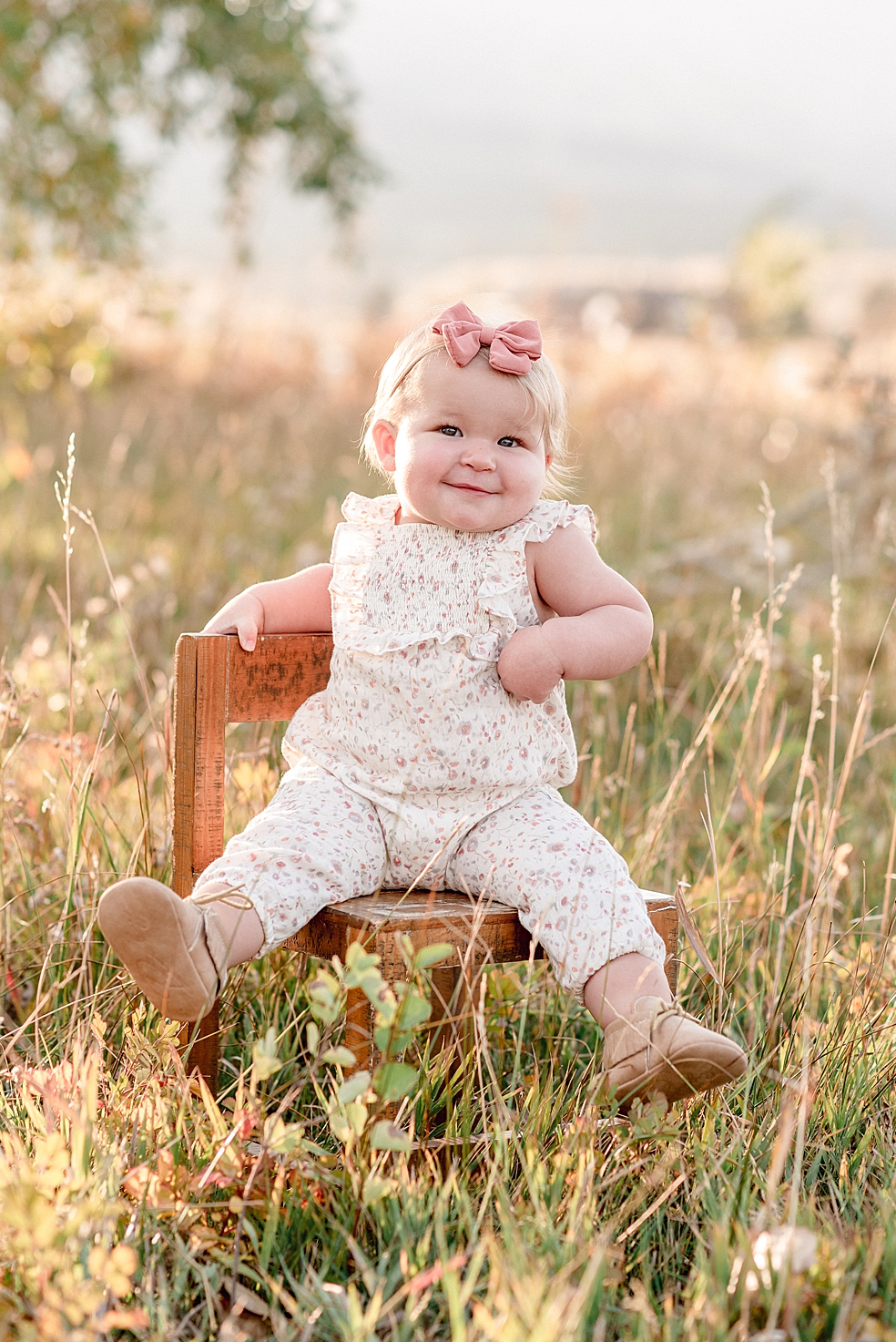 Toddler baby girl sitting on a brown chair in the grass | Photo by Jessica Lee Photography