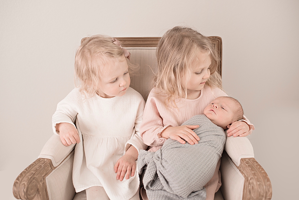 Toddler sisters in pink and cream holding their new baby brother | Photo by Jessica Lee Photography