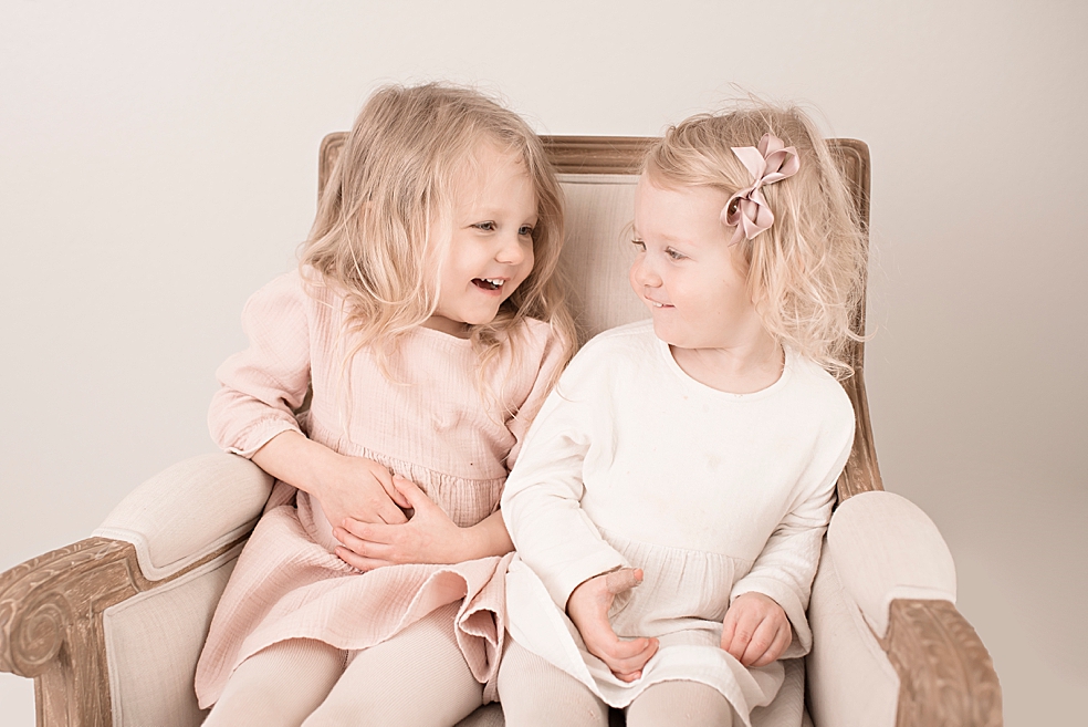 Toddler sisters in pink and white smiling at each other | Photo by Jessica Lee Photography