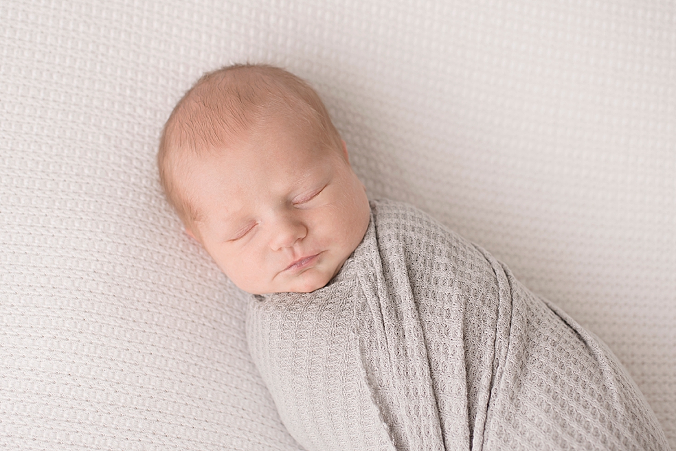 Sleeping newborn baby wrapped in gray swaddle | Photo by Jessica Lee Photography