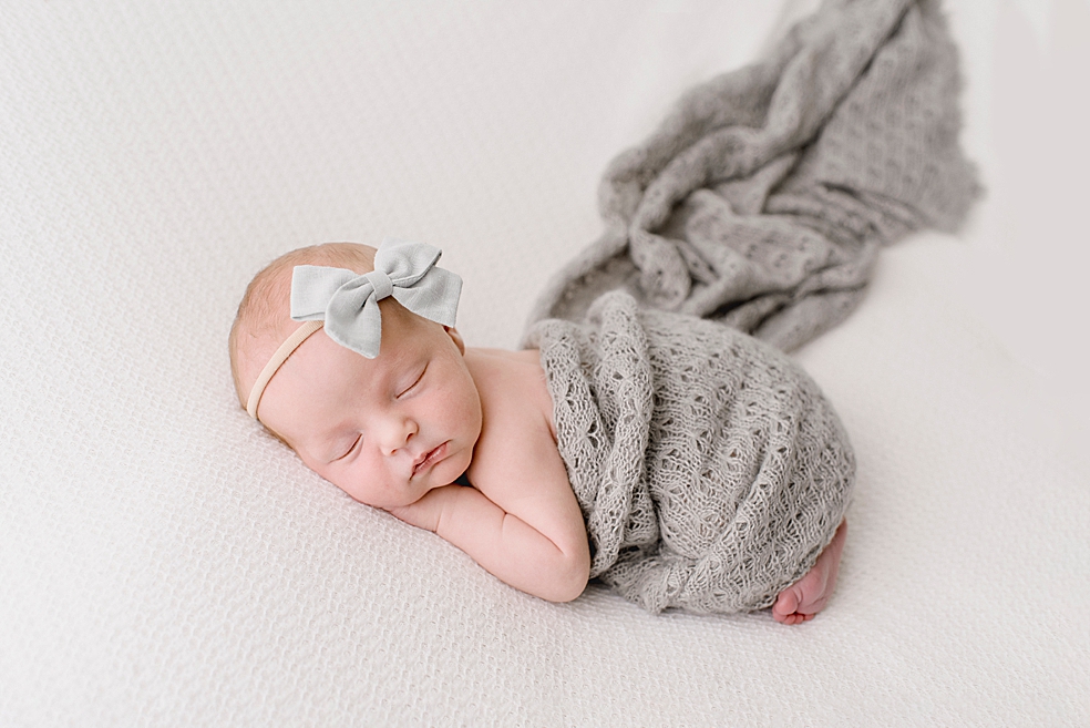 Newborn baby in gray swaddle and pale blue bow | Photo by Jessica Lee Photography