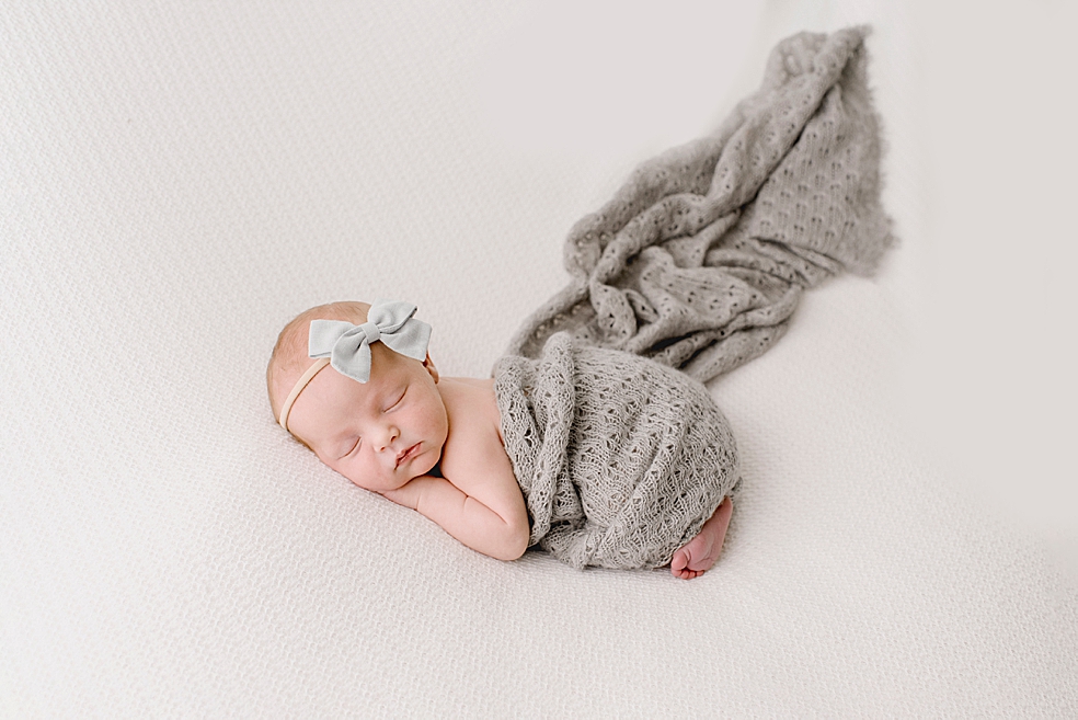Newborn baby in gray swaddle and pale blue bow | Photo by Jessica Lee Photography