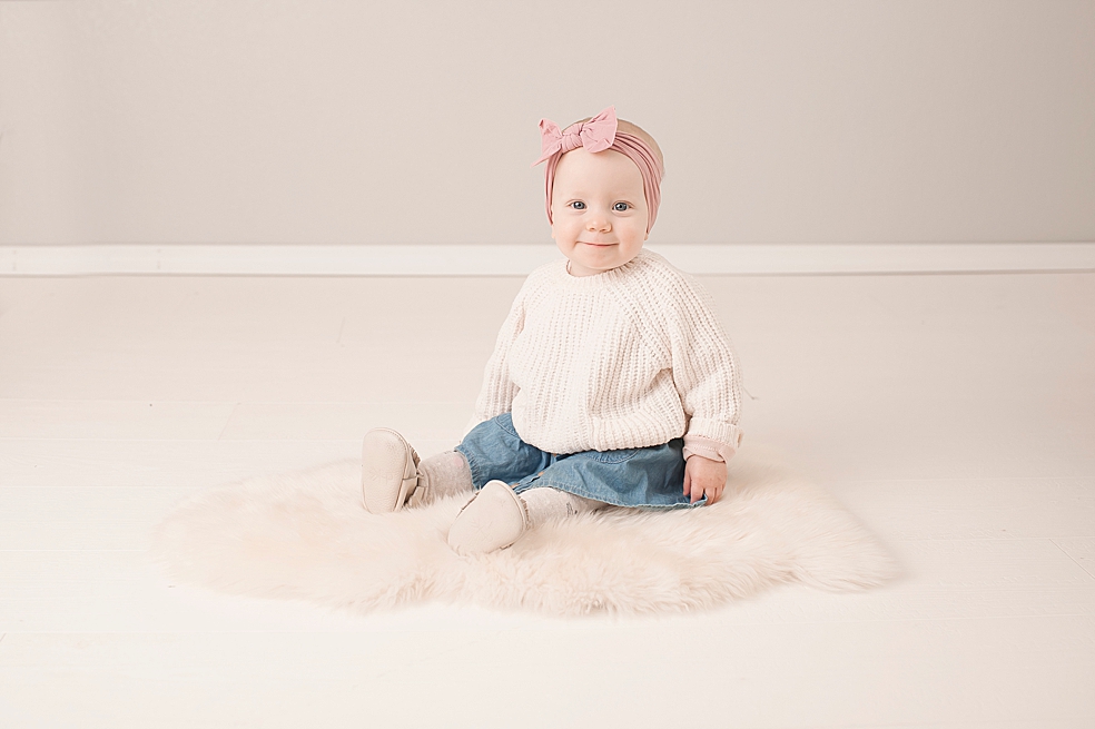 Little girl with pink bow sitting on a white rug | Photo by Jessica Lee Photography