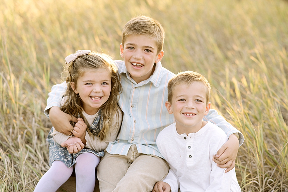 Siblings sitting together in the grass at golden light | Photo by Jessica Lee Photography 