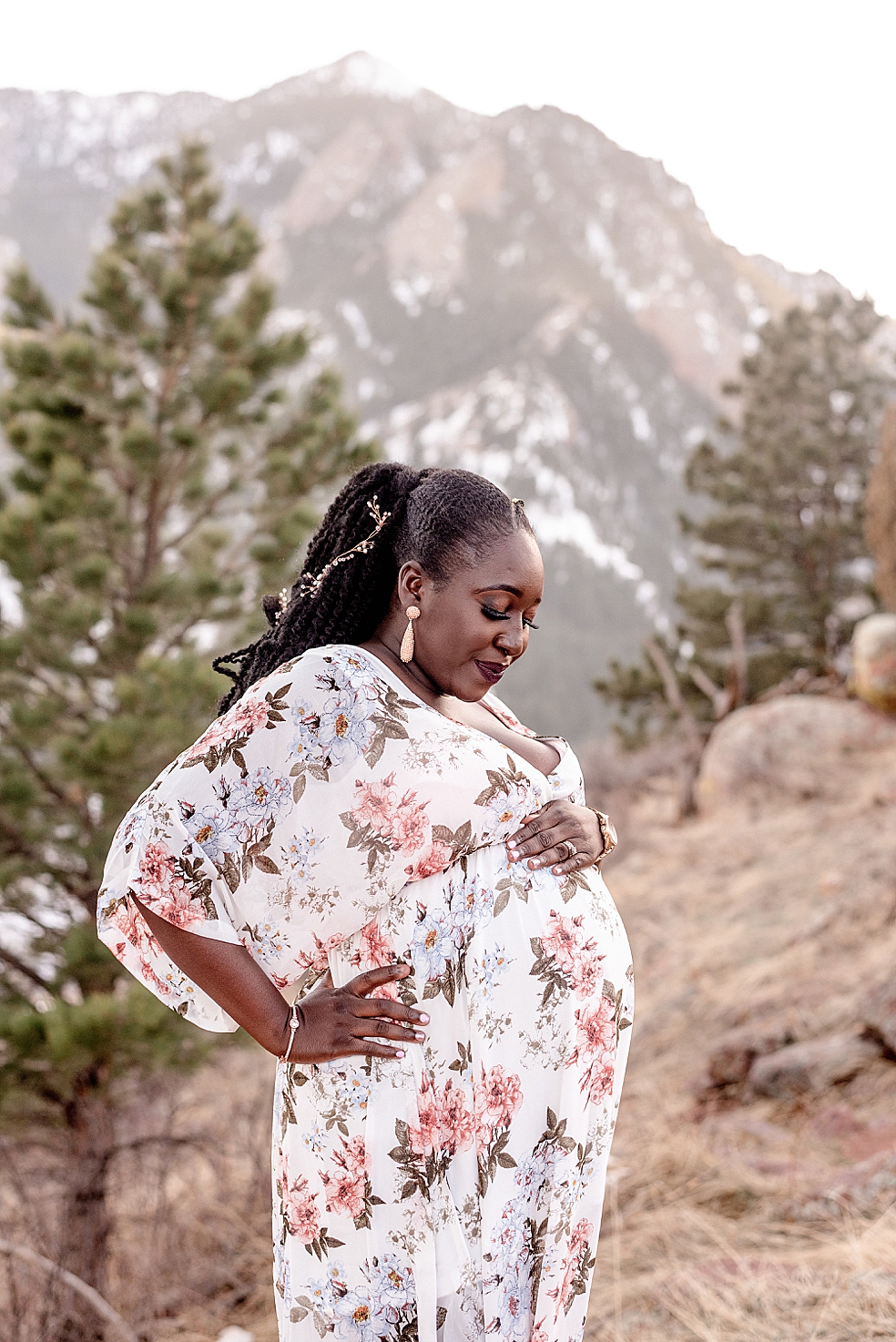 Mom to be in floral dress looking down at her belly in front of mountains | Photo by Huntsville Motherhood Photographer Jessica Lee Photography