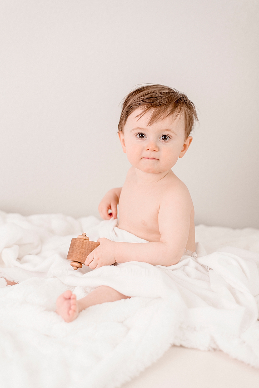 Baby boy in a white blanket playing with wooden toys | Photo by Jessica Lee Photography