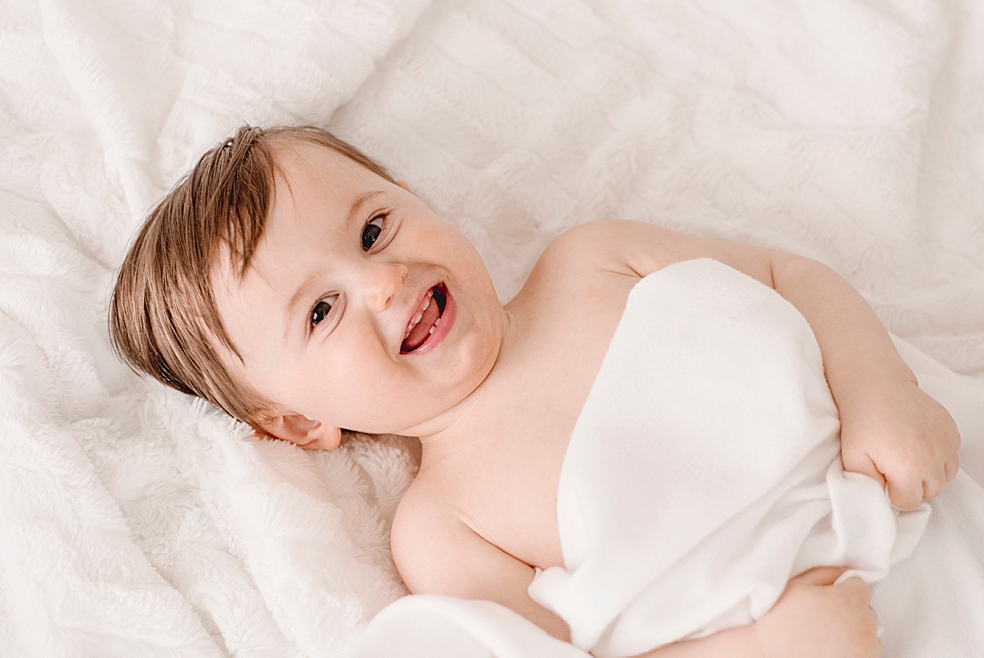 Toddler baby laughing laying on white blanket | Photo by Jessica Lee Photography