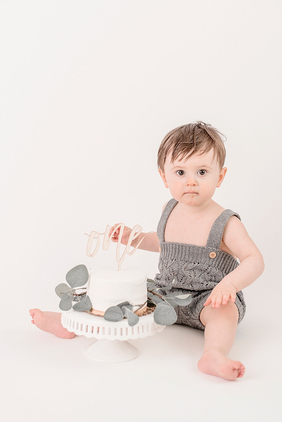 Baby boy sitting by smash cake in grab overalls | Photo by Jessica Lee Photography