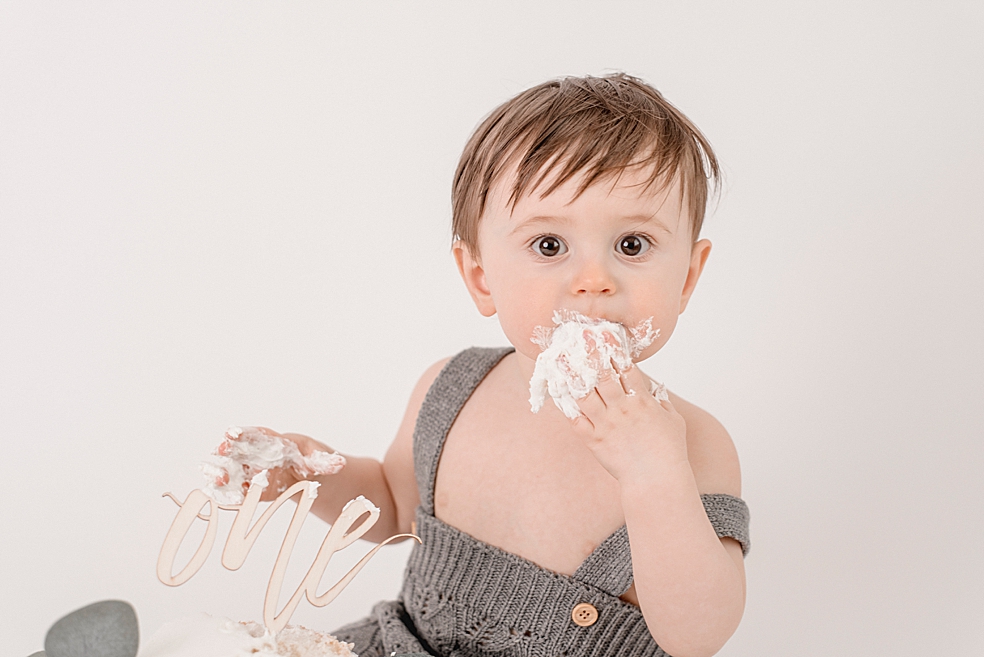 Baby boy eating cake in gray overalls | Photo by baby photographer South Huntsville Jessica Lee