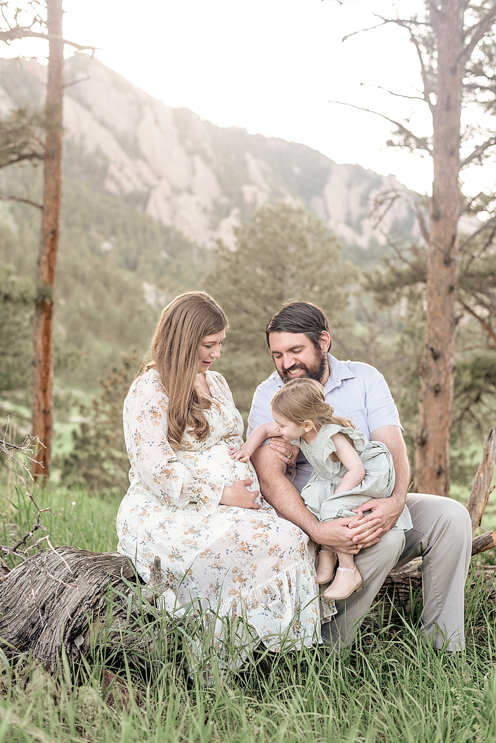 Mom and dad sitting on a log with their little girl | Photo by Jessica Lee Photography