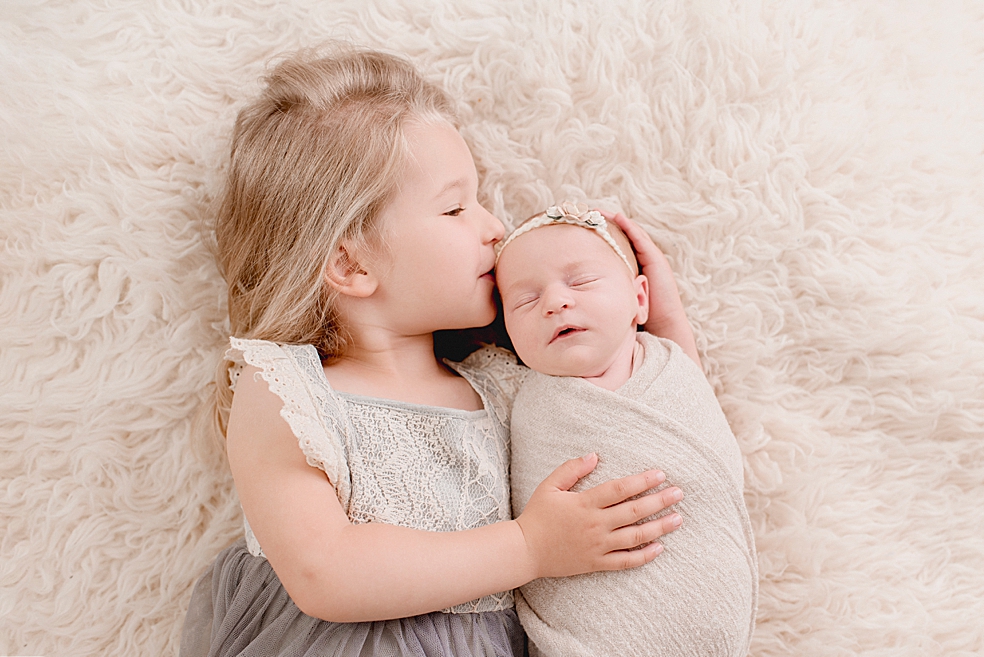 New big sister kissing her baby sister | Photo by Jessica Lee Photography