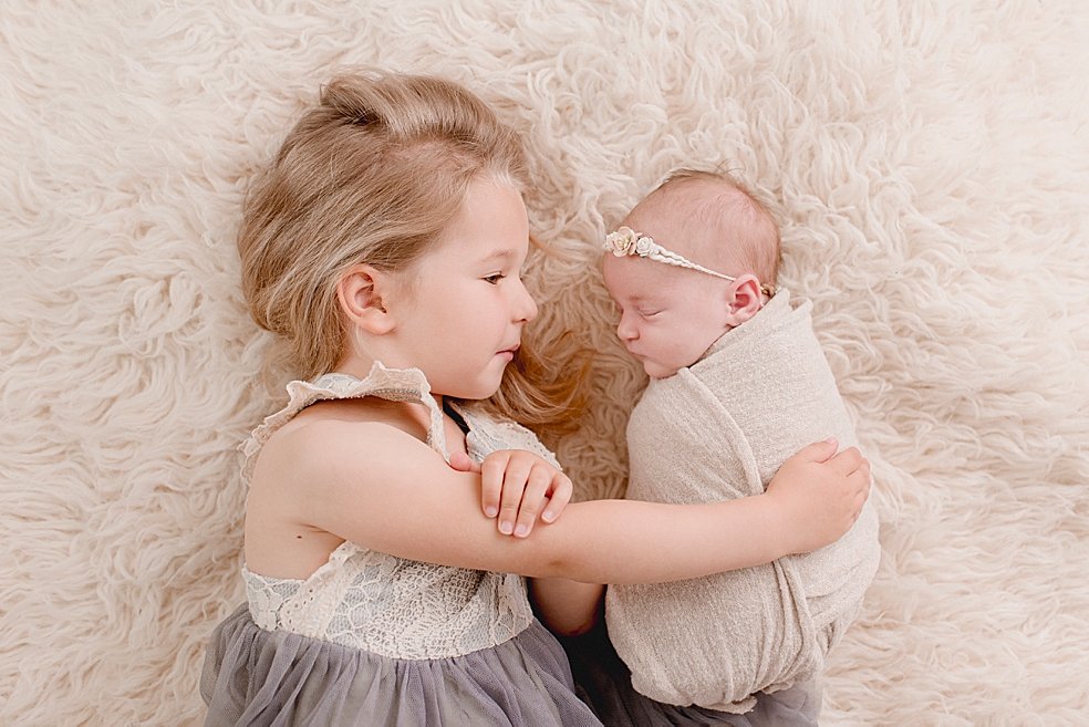 Big sister snuggling with her new baby sister | Photo by Jessica Lee Photography