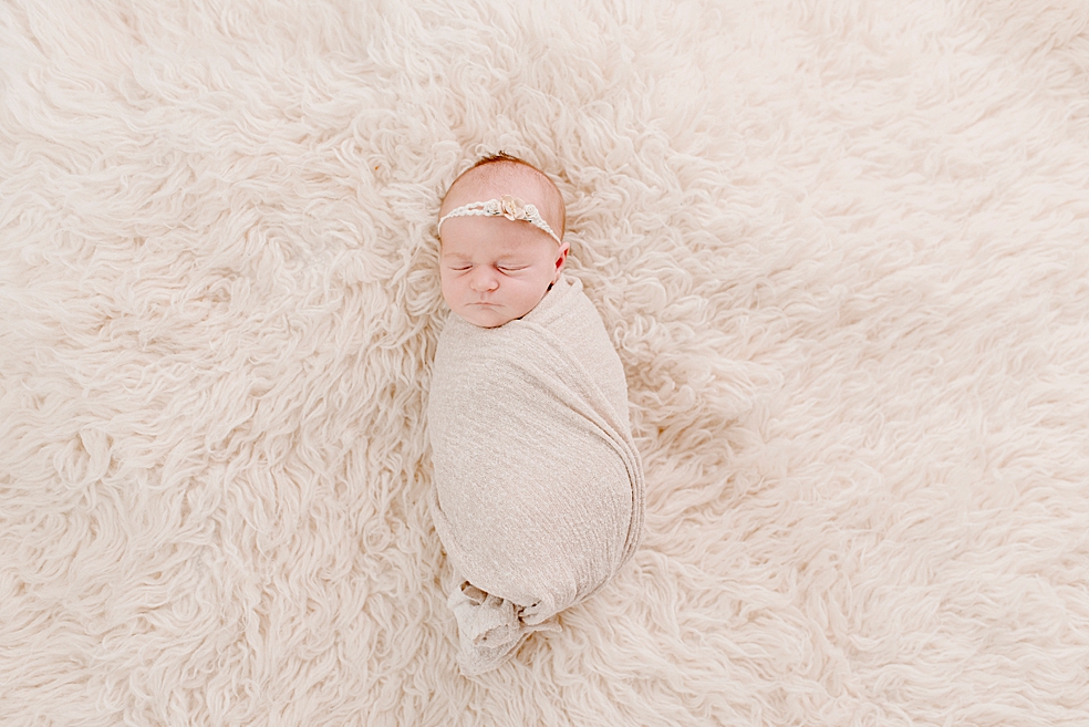 Newborn baby girl in a swaddle sleeping on a fluffy rug | Photo by Jessica Lee Photography