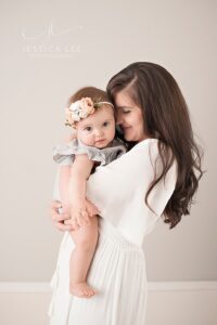 Mom in white dress holding her baby girl | Photo by Jessica Lee Photography
