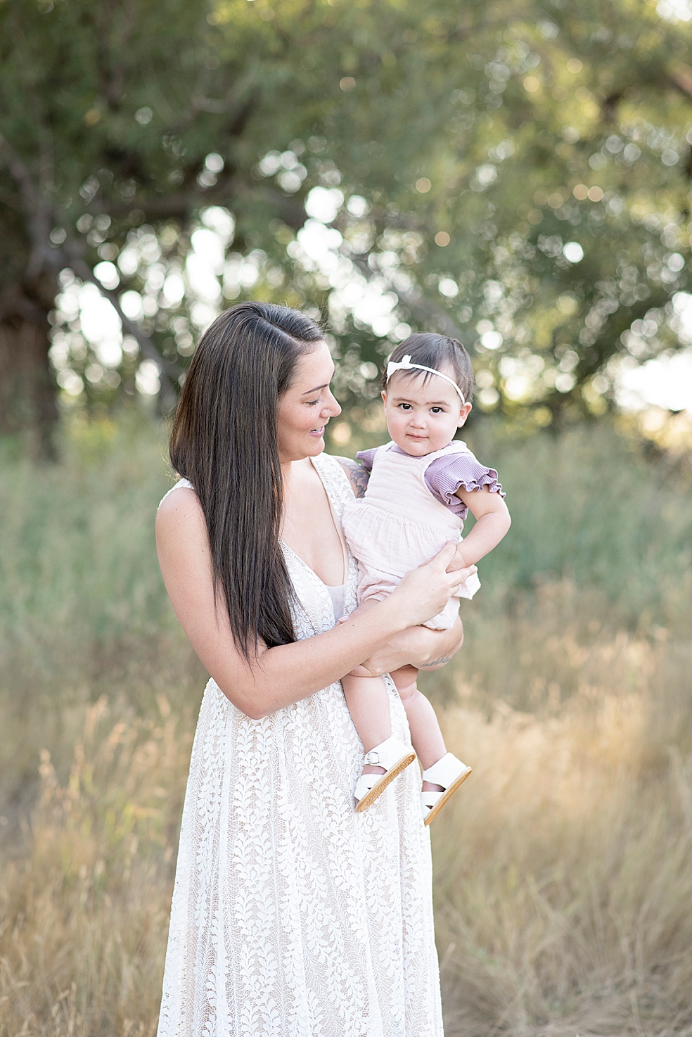 Mom in a textured white dress holding her little girl in a bow | Photo by Jessica Lee Photography