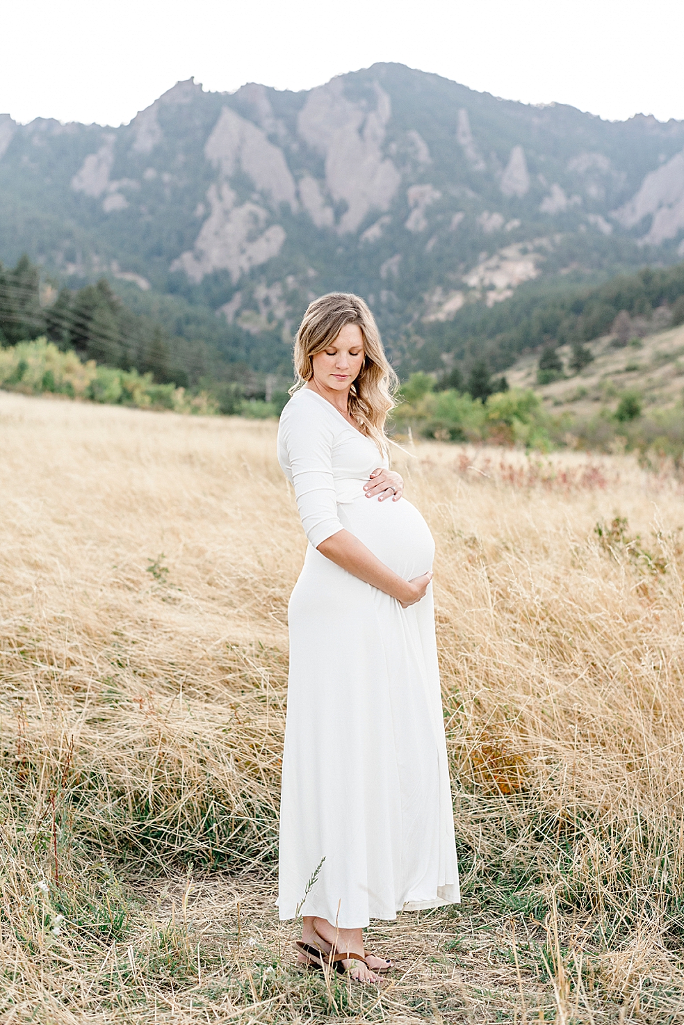 Mom to be in a long white dress holding her belly | Photo by Jessica Lee Photography