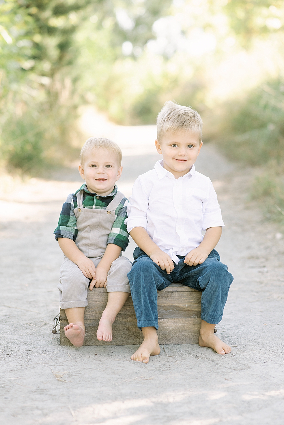Blonde brothers sitting on a box together smiling | Photo by Jessica Lee Photography