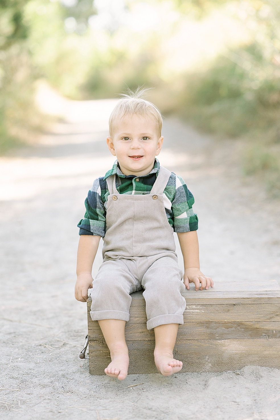 Little boy in overalls and plaid sitting on a box | Photo by Jessica Lee Photography