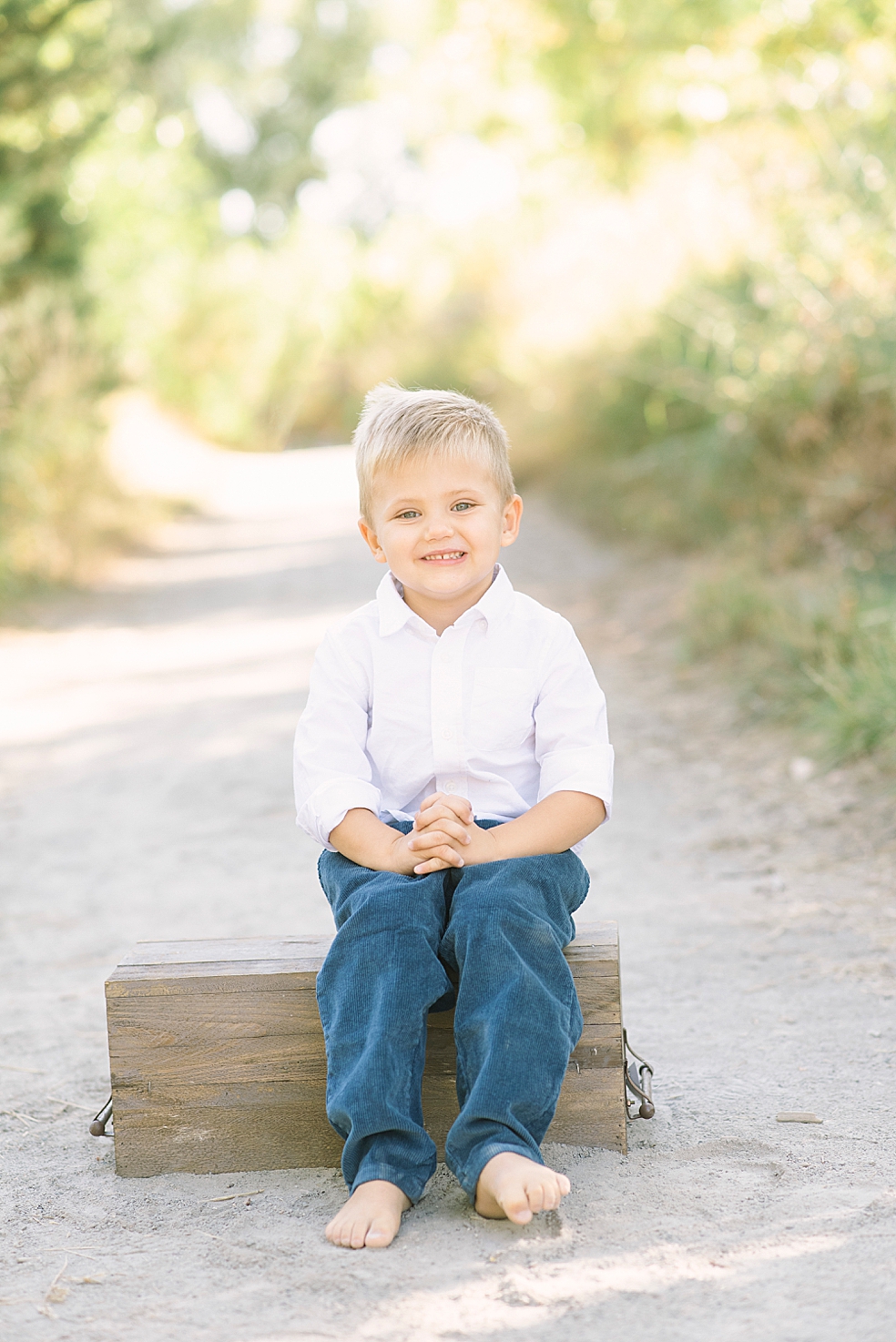 Little boy in blue and white sitting on a box on a path | Photo by Jessica Lee Photography