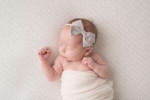 Baby girl in a gray bow wrapped in a white swaddle | Photo by Jessica Lee Photography