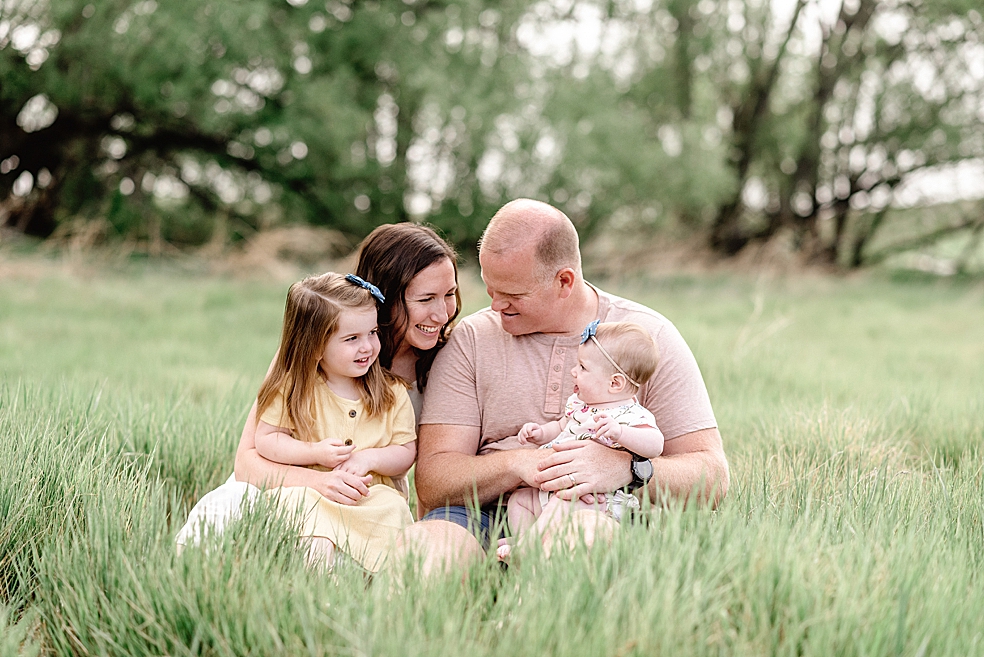 Mom and dad sitting in a field with their two daughters | Photo by Jessica Lee Photography