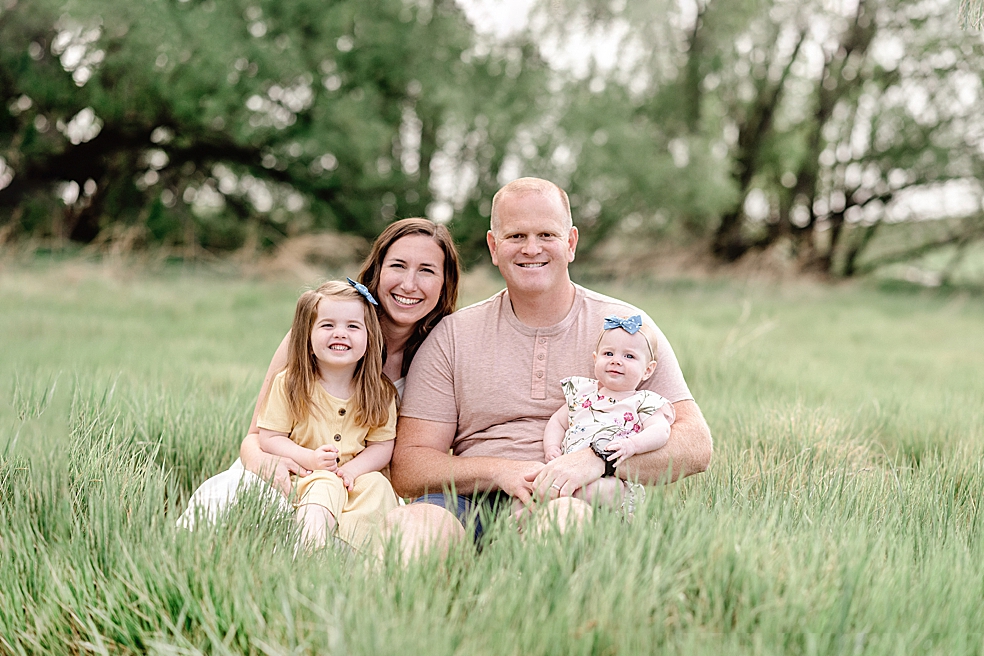 Mom and dad sitting in a field with their daughters | Photo by Jessica Lee Photography