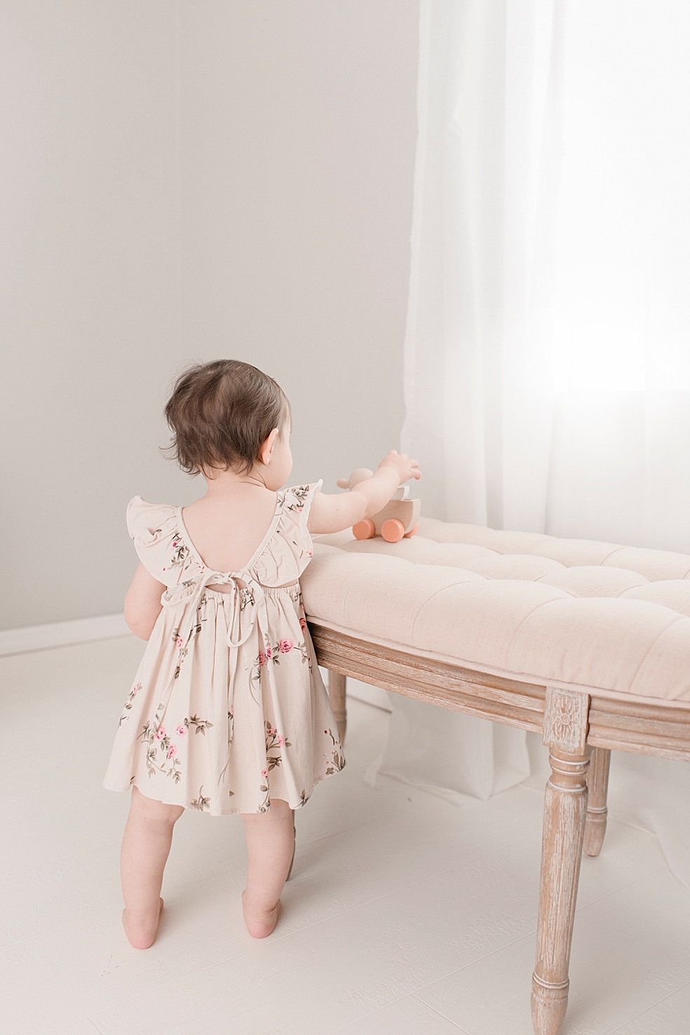 Baby girl in a floral print dress playing with a wooden duck | Photo by Jessica Lee Photography