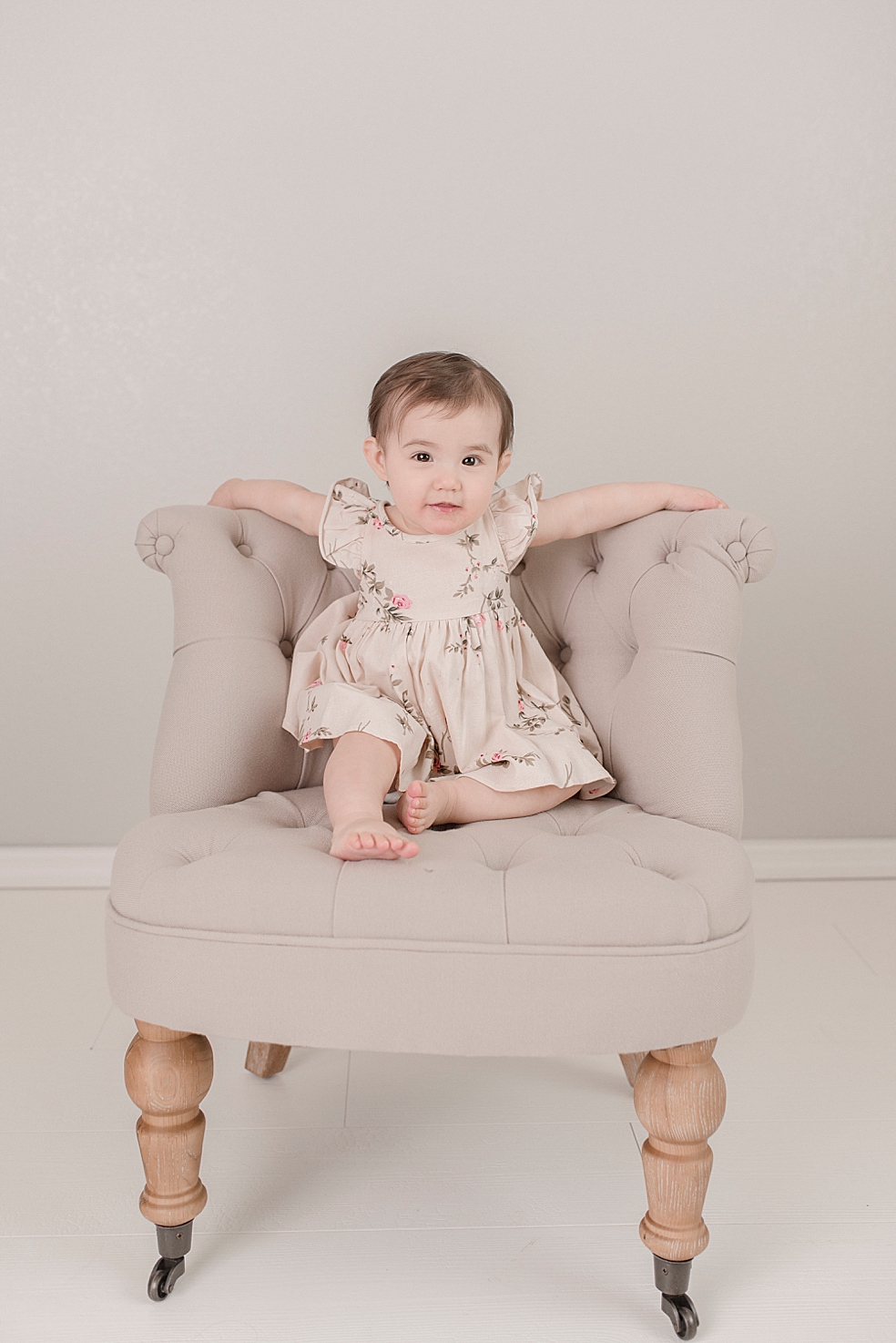 Baby girl in a floral dress sitting in a gray chair | Photo by Jessica Lee Photography