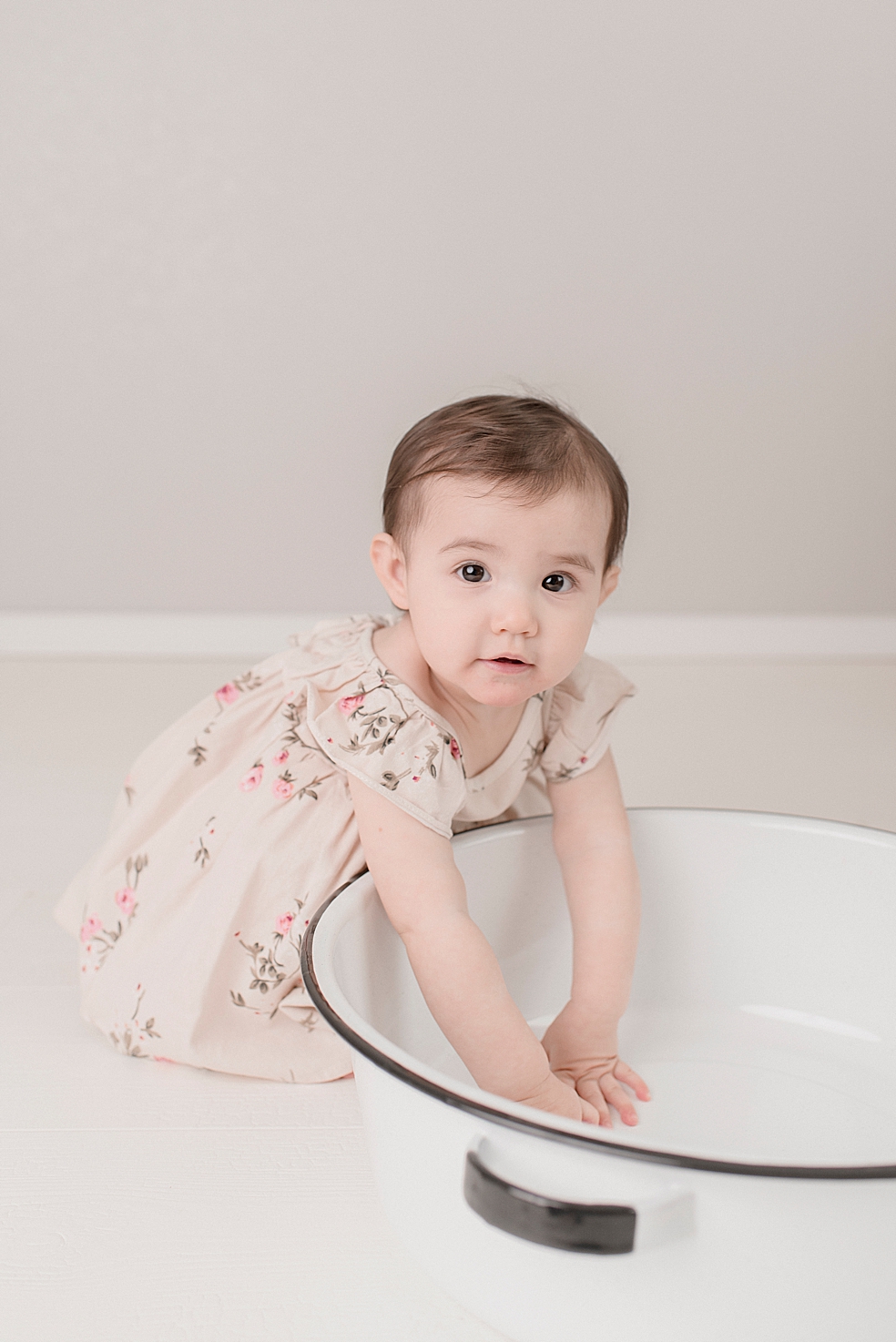 Baby girl in a floral print dress playing with a bowl | Photo by Jessica Lee Photography