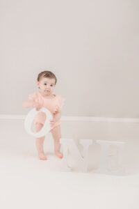 Baby girl standing with "one" letters | Photo by Jessica Lee Photography